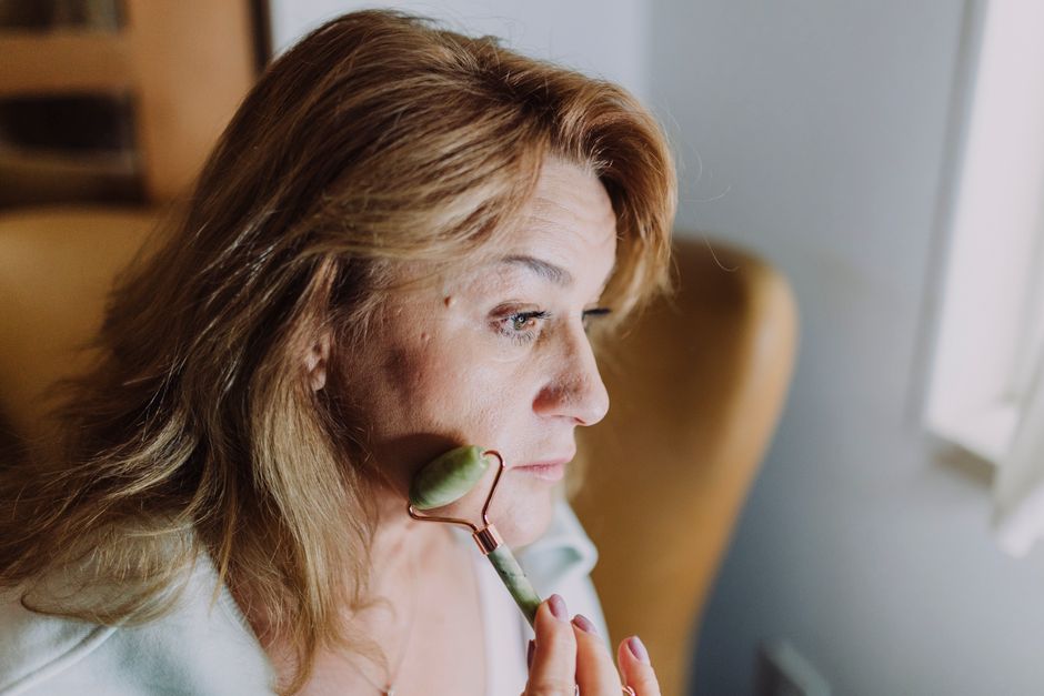 A woman using a jade roller on her face for a soothing skincare routine.