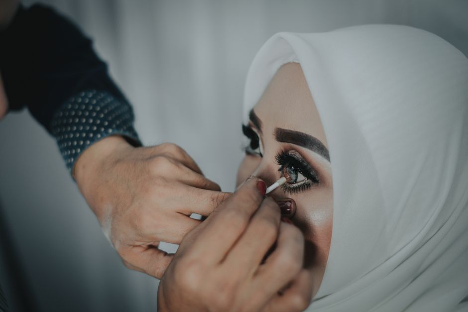 Detailed shot of eye makeup being applied to a woman wearing a hijab, showcasing cosmetic artistry.