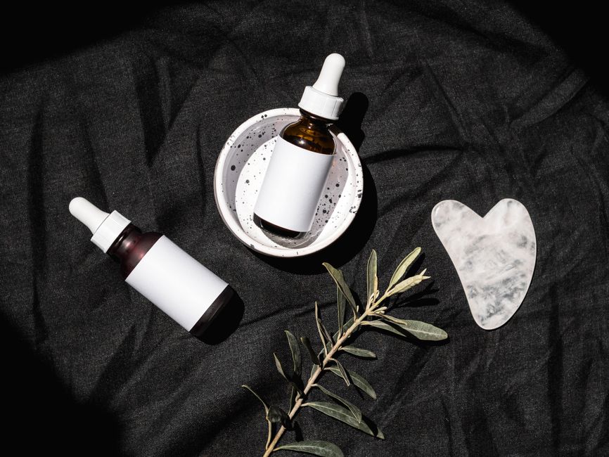 Elegant flat lay of skincare bottles and a Gua Sha stone on a dark fabric backdrop.