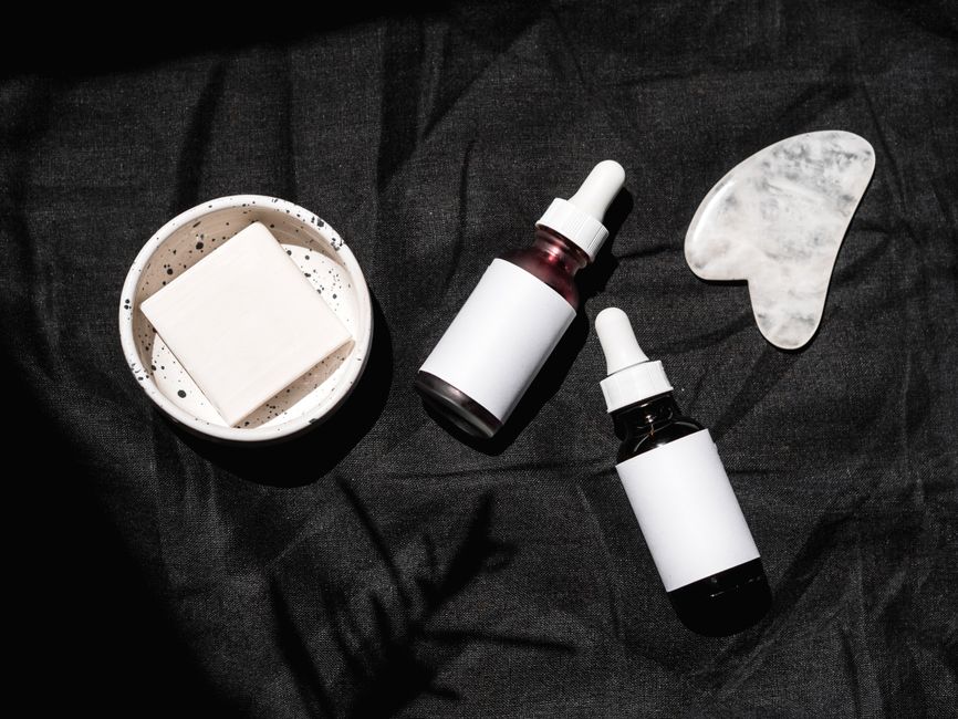 High-angle view of skincare products including serums, gua sha, and bar soap on a dark fabric backdrop.