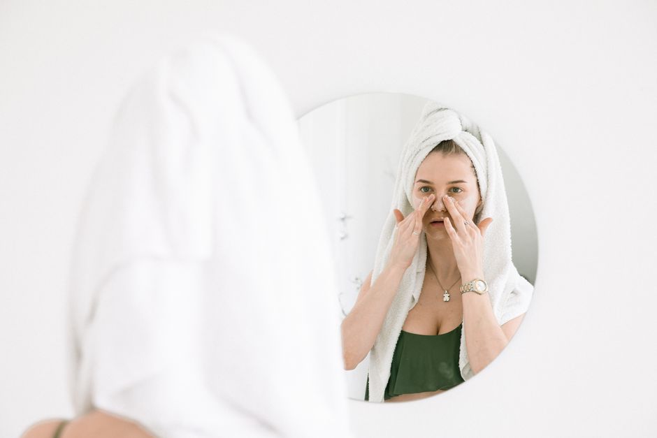 Woman applying skincare product in front of bathroom mirror