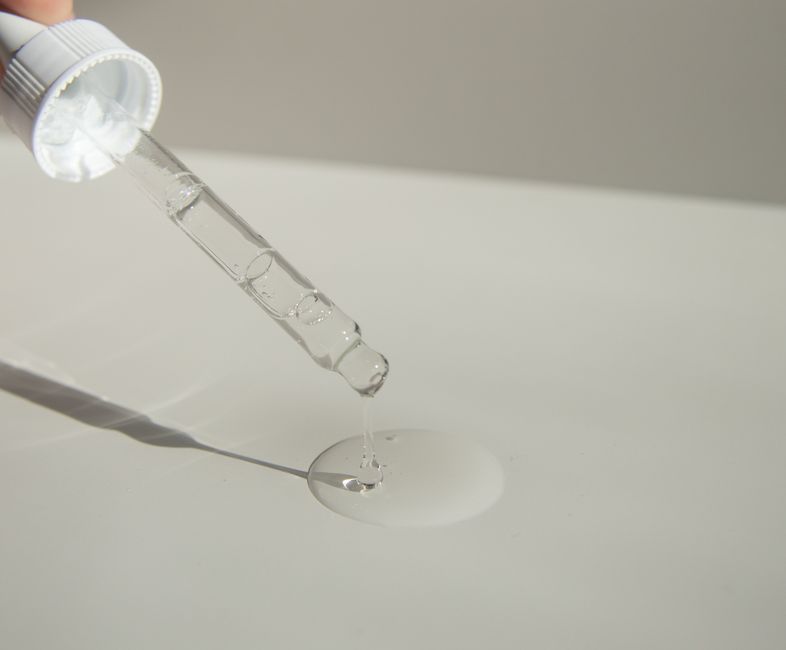 From above of crop unrecognizable person spilling transparent liquid from pipette on white table